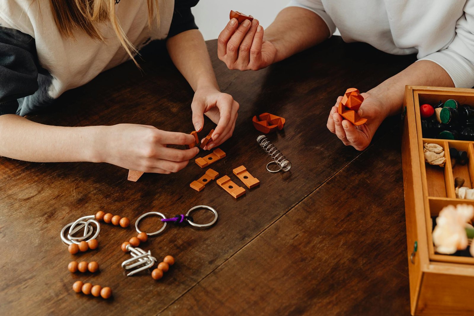 Two people cooperatively solving a wooden puzzle at a table, showcasing teamwork and creativity.
